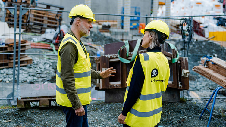 To personer i hjelm og vest fra Arbeidstilsynet som står på en byggeplass
