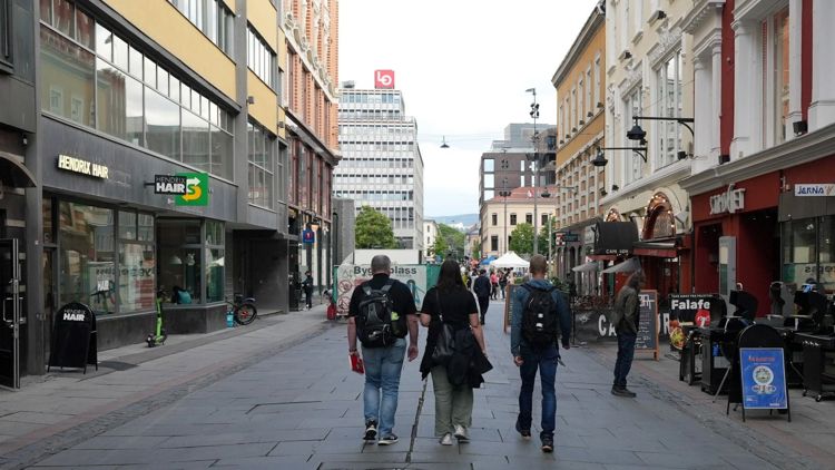 To menn og en kvinne fotografert bakfra mens de  spaserer i en gate med mange bygninger rundt.