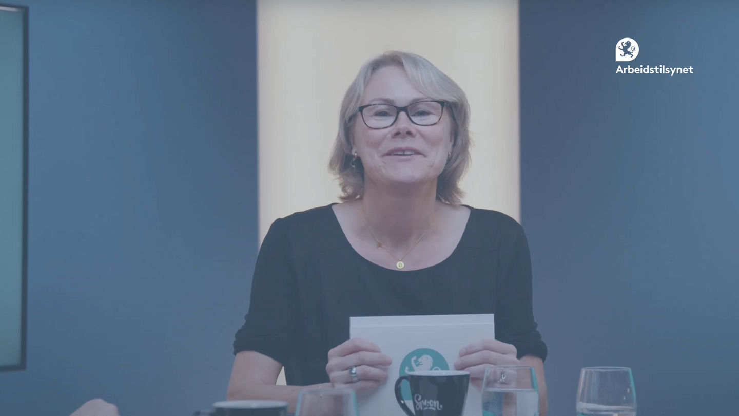 Bilde fra webinaret av programleder Christin. Hun sitter ved et bord, har talekort i hendene, snakker og ser rett i kamera.