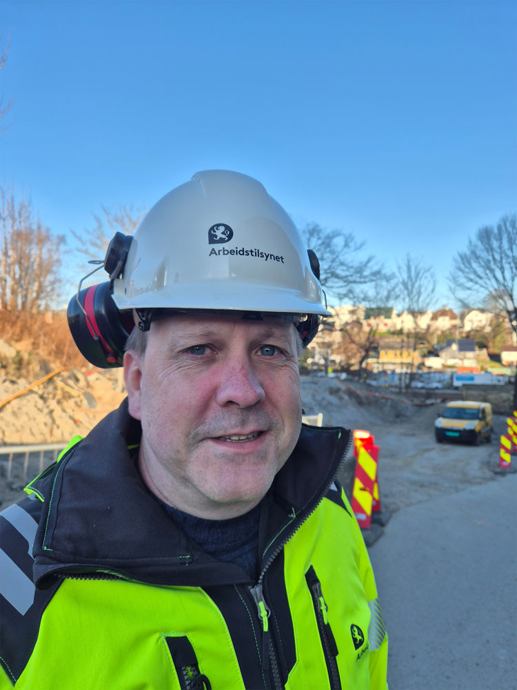 Mann i arbeidsklær og hjelm ser i kamera
