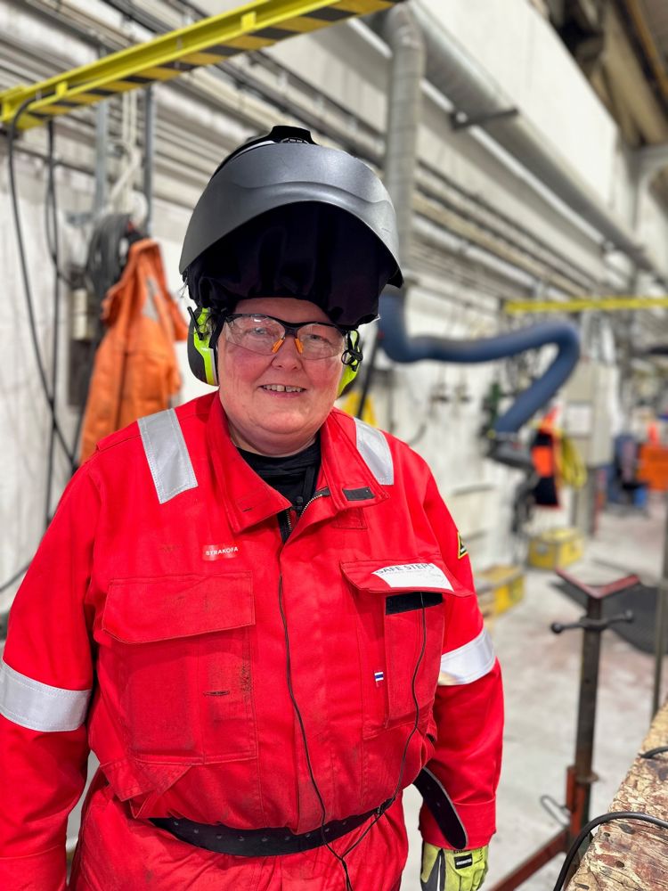 Kvinne i arbeidsklær og sveisemaske i en industrihall