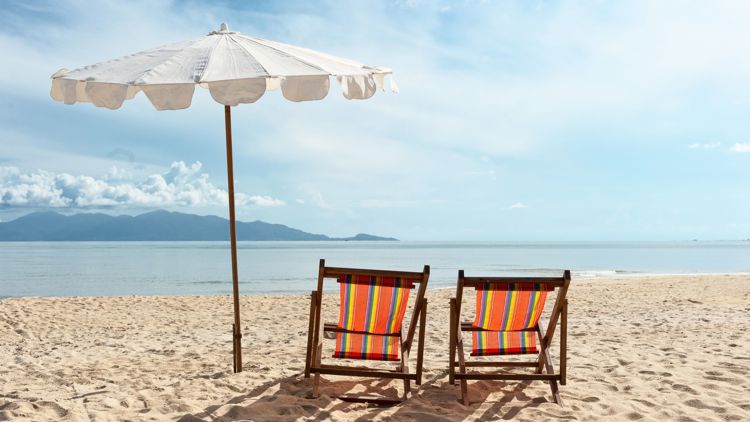 Bildet viser en strand med to solstoler og en parasoll. 